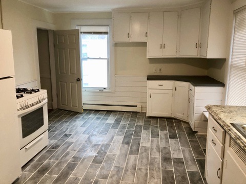 Renovated kitchen with white cabinets, gray plank flooring, and shiplap at 36 Pratt Street