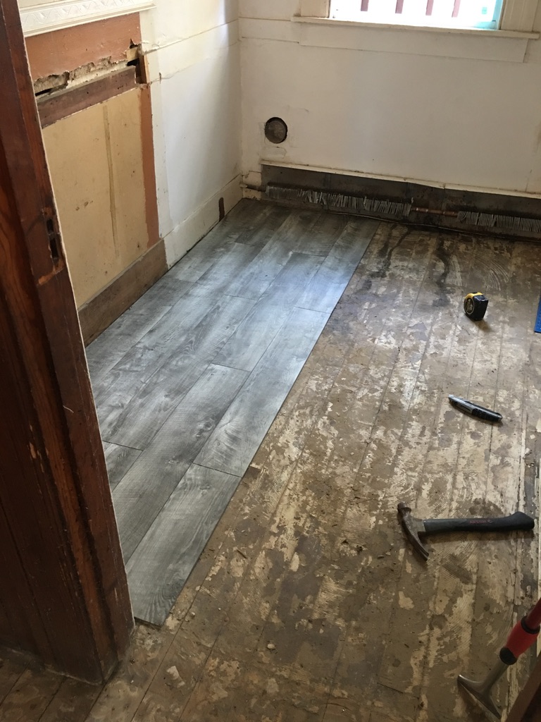 Gray vinyl plank flooring being installed over an old wood subfloor at 31 Wallace Street